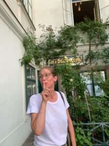 Frau mit Finger an den Lippen in einem begrünten Wiener Innenhof vor einem versteckten Café