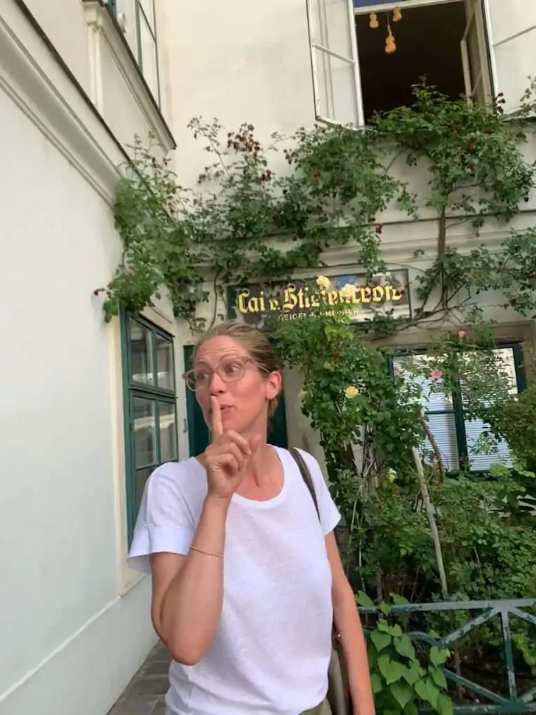 Frau mit Finger an den Lippen in einem begrünten Wiener Innenhof vor einem versteckten Café