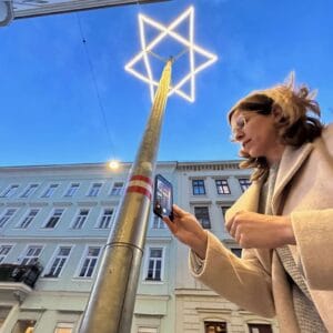 Frau fotografiert einen beleuchteten Davidstern auf einer Säule in einer Wiener Straße
