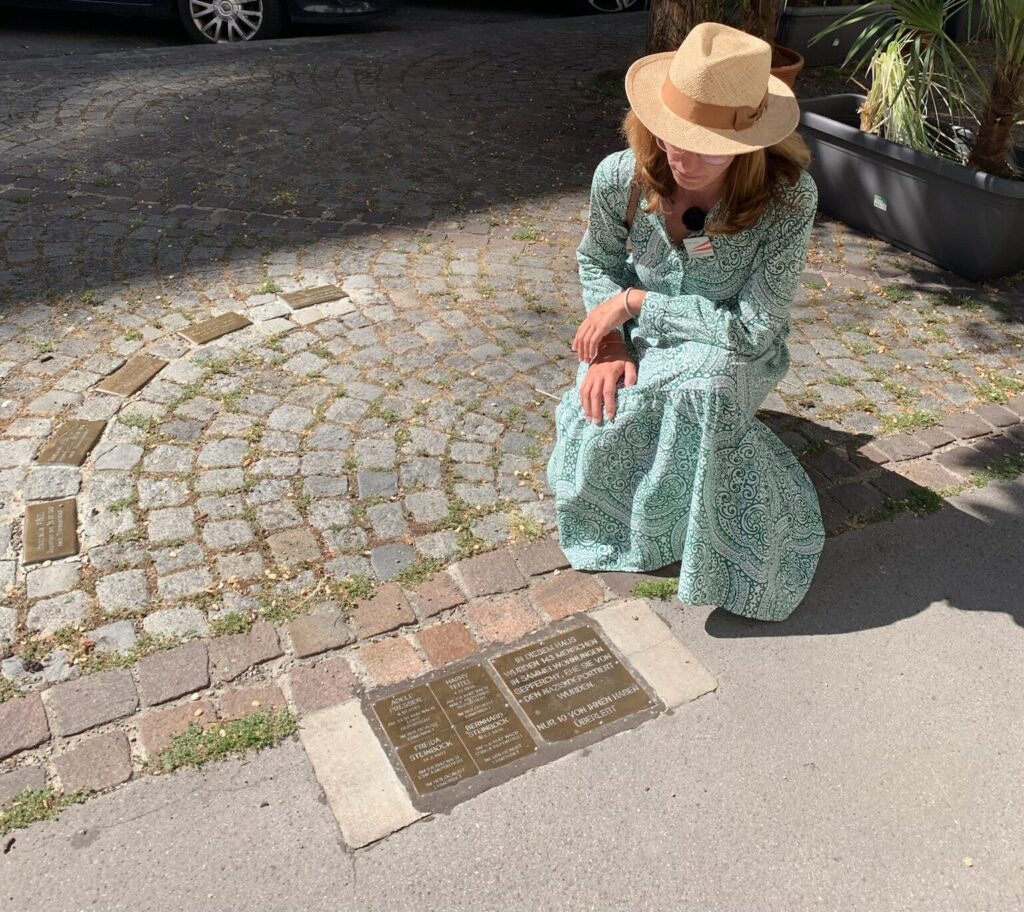 Martha Tretter kniet in einer Wiener Gasse vor vier Steinen der Erinnerung im Pflaster