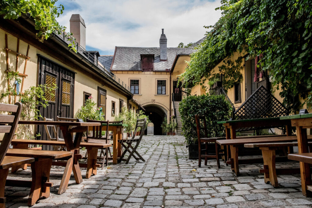 Begrünter Innenhof des Heurigen mit Holztischen und Kopfsteinpflaster